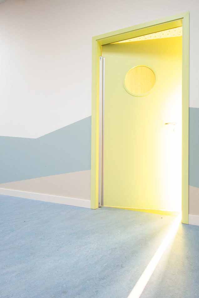 Gelbe Innentür mit rundem Sichtfenster. An der Wand neben der Tür zieht sich ein hellblauer Streifen. Der Boden ist im gleichen Blauton.
